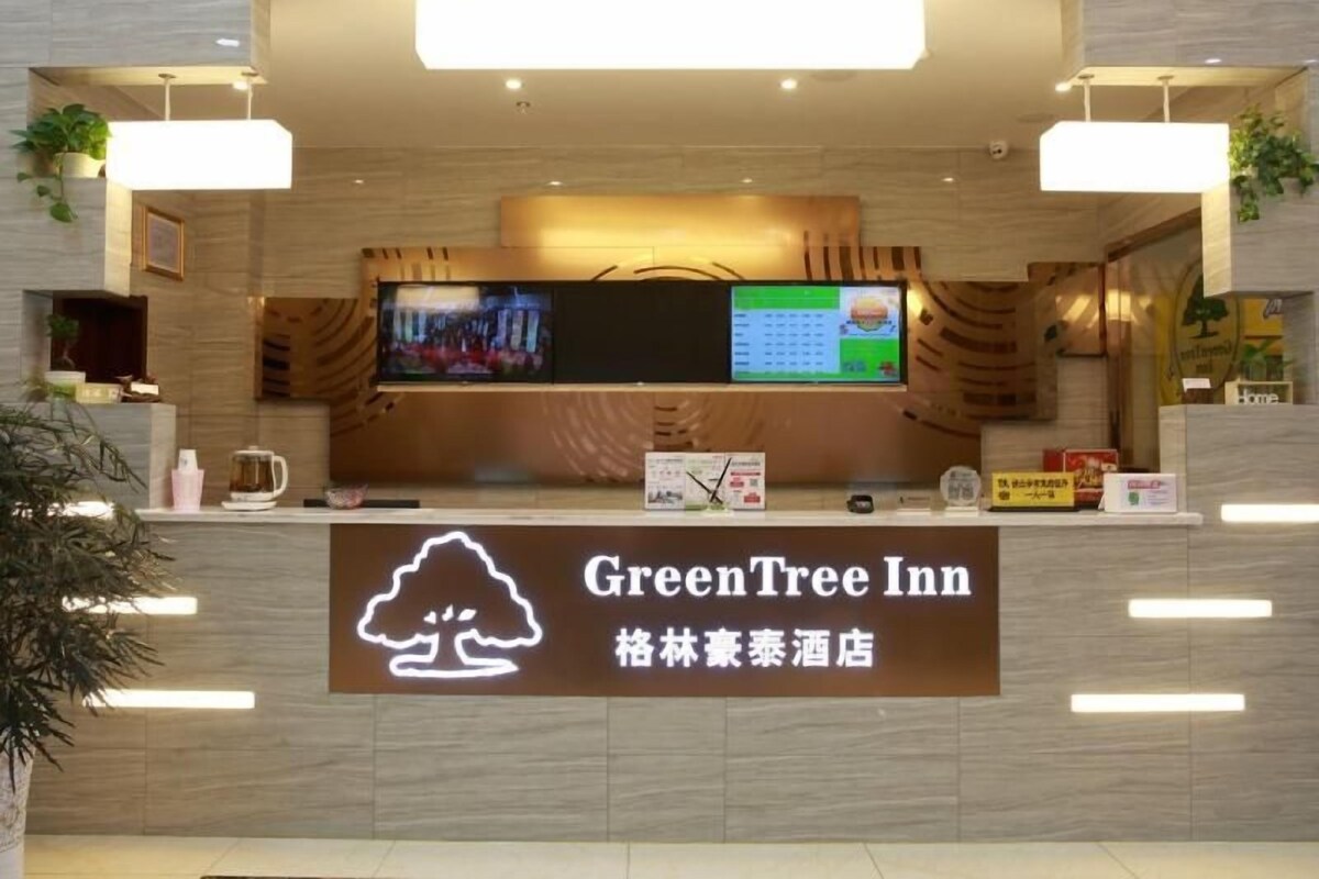 A reception area with a digital display, a sign for GreenTree Inn, and a logo of a tree.