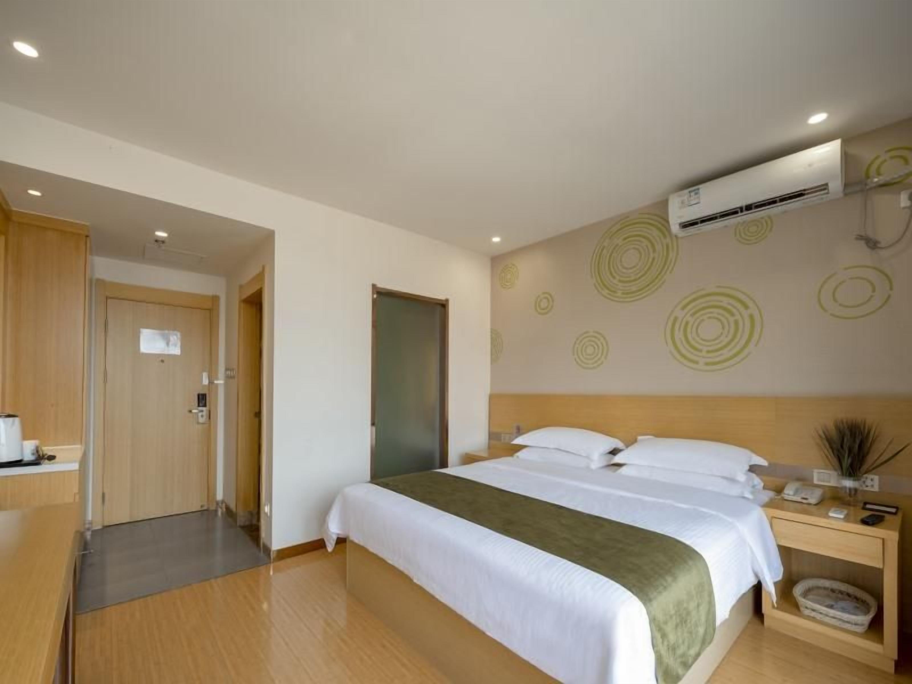 A hotel room with a bed, bedside table, and an air conditioning unit.