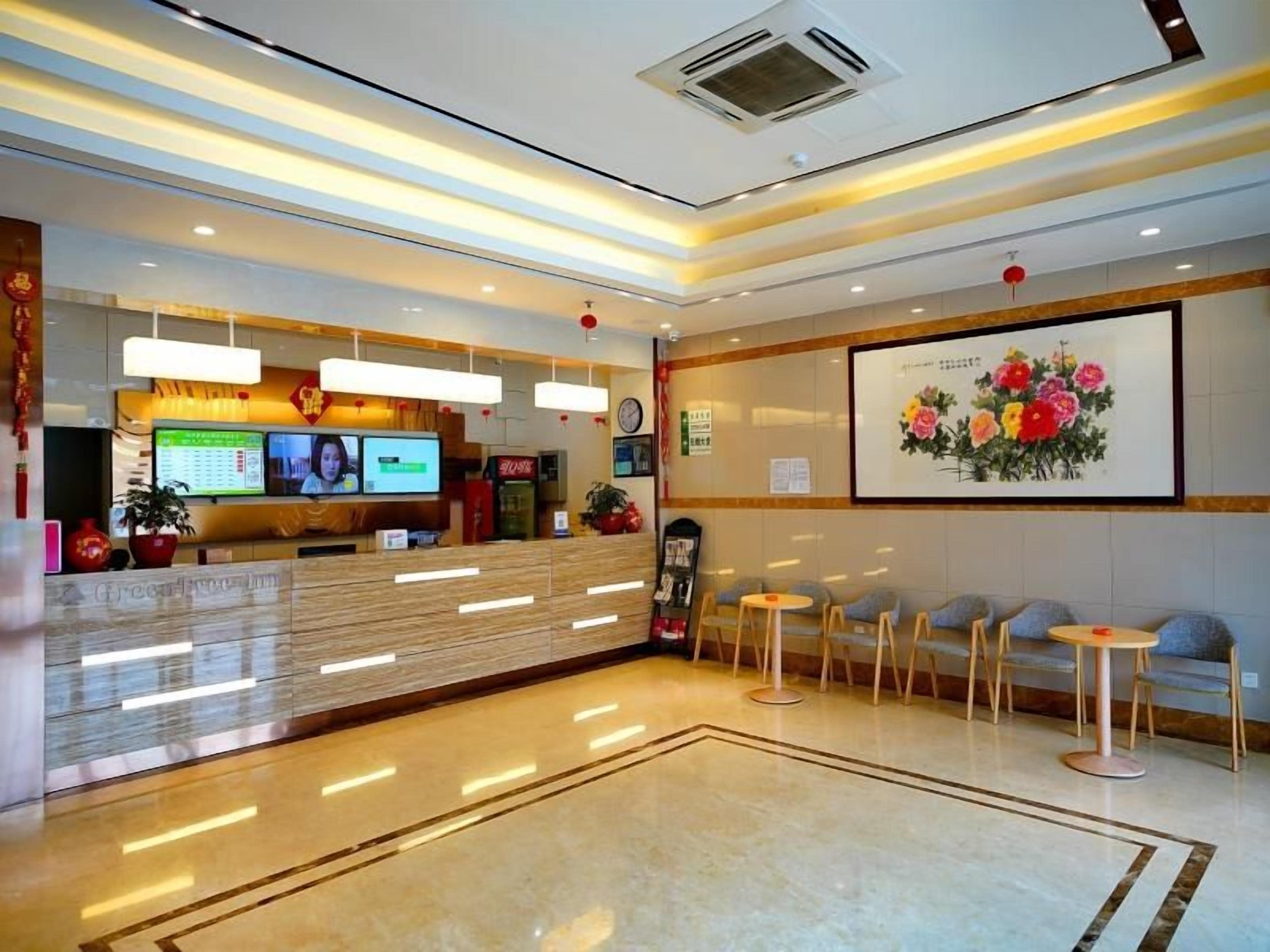 Ein Hotel-Rezeptionsbereich mit einem digitalen Display, Sitzgelegenheiten und einem Blumenbild an der Wand.