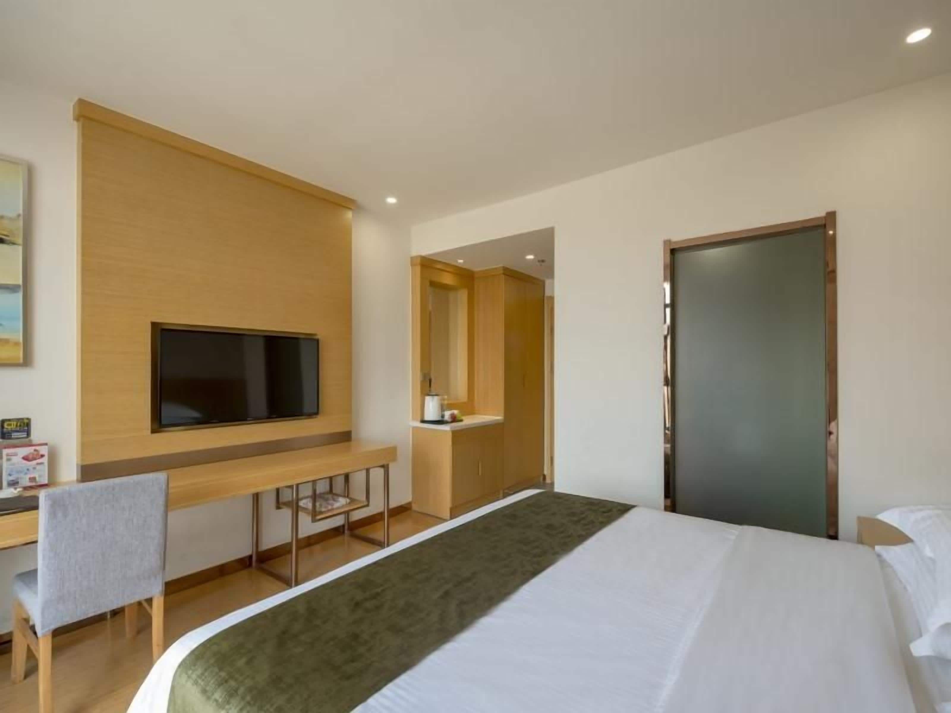 A hotel room with a bed, a desk with a chair, a television, and a mirror.