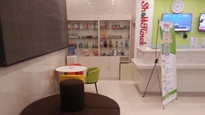 A modern interior with a reception desk, a seating area with a round table, and a display of products on shelves. - Shell Xizhou Xifu District West Heping Street Hotel (Xinzhou)