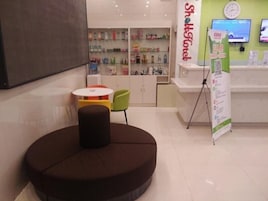 A modern interior with a reception desk, a seating area with a round table, and a display of products on shelves.