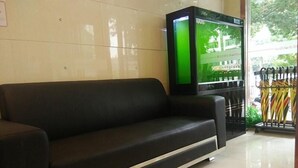 A black sofa in a hotel lobby with a tiled floor and a green screen TV mounted on the wall. - Shell Xizhou Xifu District West Heping Street Hotel (Xinzhou)