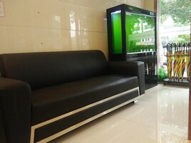 Un sofá negro en el vestíbulo de un hotel, con piso de baldosas y un televisor de pantalla verde montado en la pared.