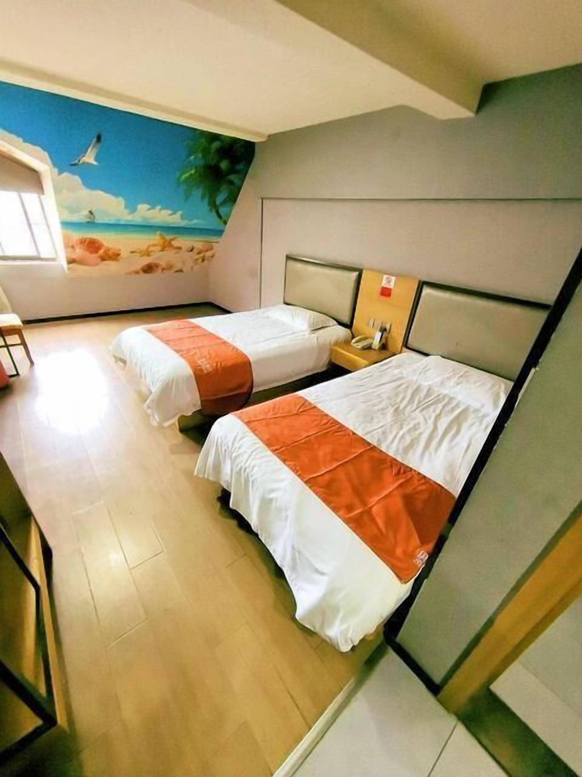 Une chambre d’hôtel avec deux lits, une fresque représentant une scène de plage et un plancher en bois.