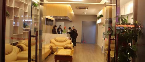 A hotel lobby with a reception desk, leather sofas, a coffee table, and glass display cases.