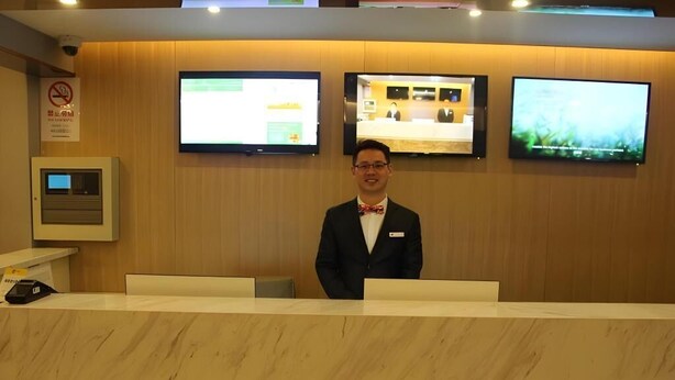 A reception desk with a wooden panel wall, two monitors, and a no-smoking sign. - Shell Shanghai Chedun Yingshi City Yingshi Road Hotel (Shanghai)