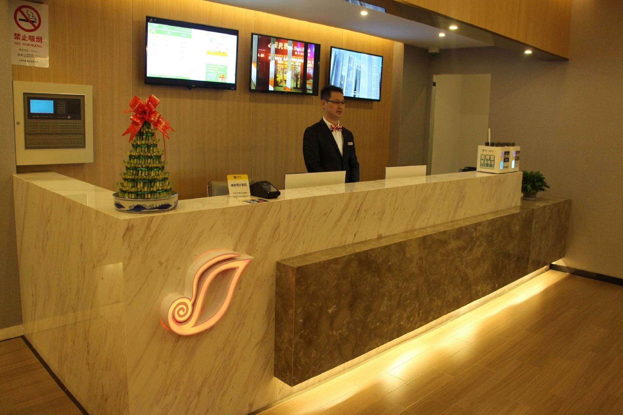 A hotel reception desk with a digital screen, a no-smoking sign, and a decorative Christmas tree.