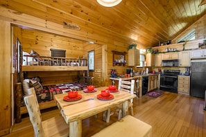 A wooden cabin interior with a dining table set for four, a kitchen with modern appliances, and a cozy seating area. - 84° Private Indoor Heated POOL, Arcade, Views, Sauna, Hot Tub, 300MB WIFI (Sevierville)