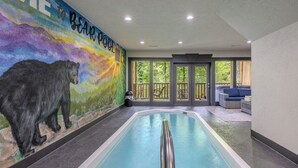 Una piscina interior con un mural de un oso, un área de descanso con vistas al exterior e iluminación empotrada en el techo.