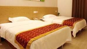 Habitación de hotel con dos camas, cada una con ropa blanca y detalles decorativos rojos. Cuenta con un cabecero de madera, un teléfono montado en la pared y un cuadro sobre las camas.