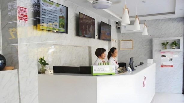 Un mostrador de recepción con dos empleados, una pared de mármol, cuadros enmarcados y una planta pequeña.
