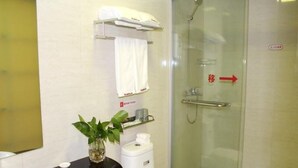 Un baño con cabina de ducha de vidrio, inodoro blanco, encimera negra con lavabo y una planta en maceta.