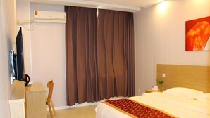 Habitación de hotel con cama, escritorio, silla, aire acondicionado y un cuadro en la pared.