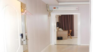 Un pasillo con una puerta blanca, un perchero y una habitación al fondo con una cortina y una pequeña mesa.