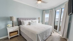Un dormitorio con cama, mesitas de noche, ventilador de techo y vistas al exterior.
