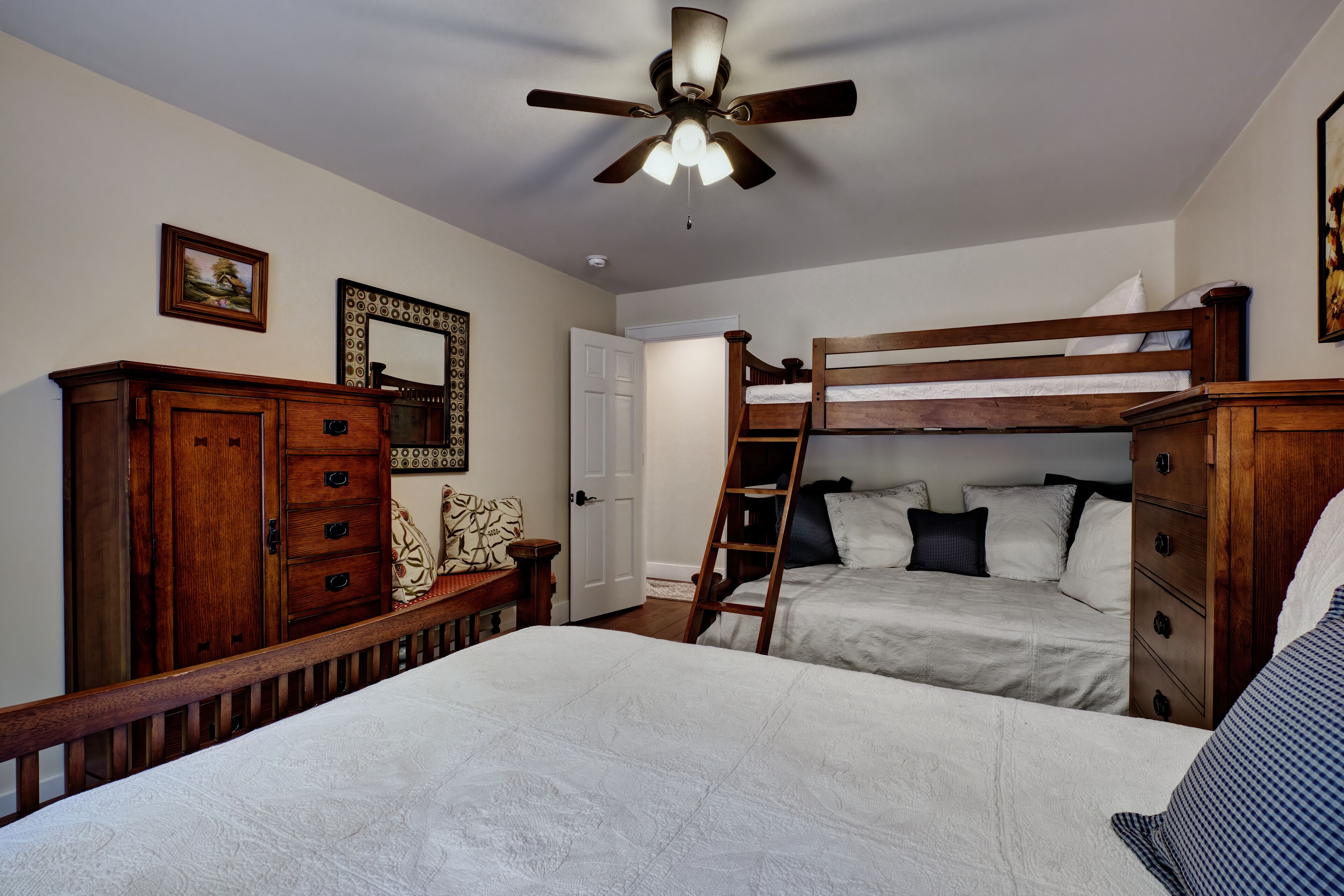 A bedroom with two beds, a wooden dresser, a mirror, and a ceiling fan.