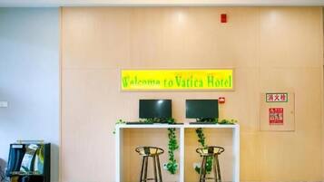 A reception desk with a 'Welcome to Vatica Hotel' sign, two monitors, and two bar stools.