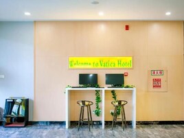 Una recepción con un cartel que dice 'Welcome to Vatica Hotel', dos monitores y dos taburetes de bar.