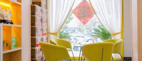 A room with a yellow chair, a shelf with books, and a window with a curtain.
