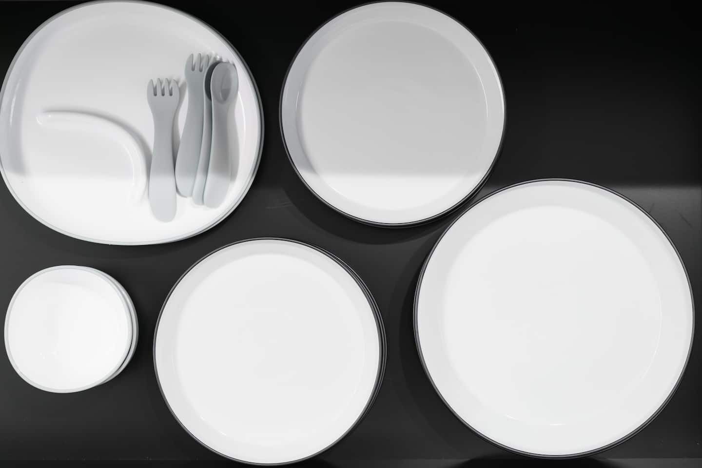 A set of white plates and cutlery arranged on a black surface.