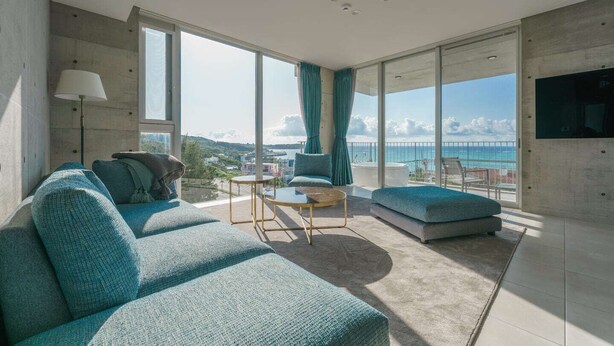 A modern living room with a large sofa, a coffee table, and a view of the ocean. - Okinawa Plaisant Villa (Onna)