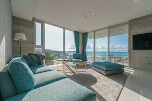 A modern living room with a large sofa, a coffee table, and a view of the ocean. - Okinawa Plaisant Villa (Onna)