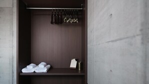 A hotel room with a wardrobe containing folded towels, a hanging rack with keys, and a small shelf with a bottle and a container. - Okinawa Plaisant Villa (Onna)
