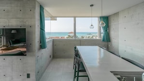 A modern kitchen with a large window, a dining area, and a view of the ocean. - Okinawa Plaisant Villa (Onna)