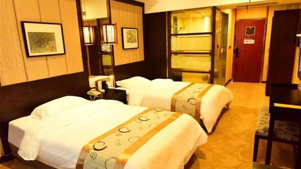 Habitación de hotel con dos camas, un escritorio, una silla, un armario y un baño visible a través de una puerta abierta.