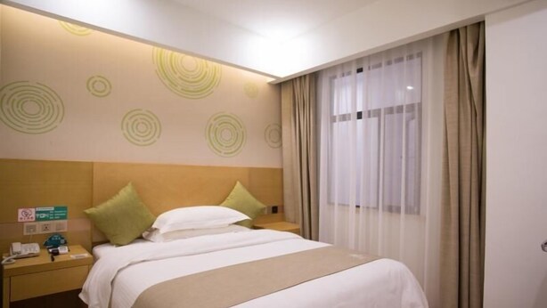 Una habitación de hotel con cama, mesita de noche, cubo de basura y ventana con cortinas.