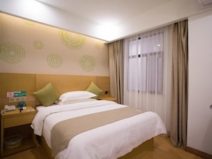 Quarto de hotel com cama, mesa de cabeceira, lixeira e janela com cortinas.