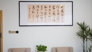 Una habitación con dos sillones color beige, una pequeña mesa de madera con una planta en maceta, y una gran obra de caligrafía enmarcada en la pared.