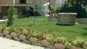 A two-story building with a balcony, a garden with flowers and a small tree, and a stone structure. - B&B La Tartaruga (Civitanova Marche)