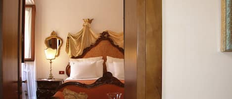 A hotel room with a bed, a bedside table with a lamp, a chandelier, and a red carpet.