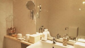 A bathroom with a sink, mirror, towel dispenser, and toiletries.