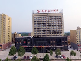 A multi-story hotel with a large sign on the top, a parking lot in front, and several trees around the building.