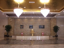 A lobby with a marble floor, a stone wall with artwork, and two chandeliers.