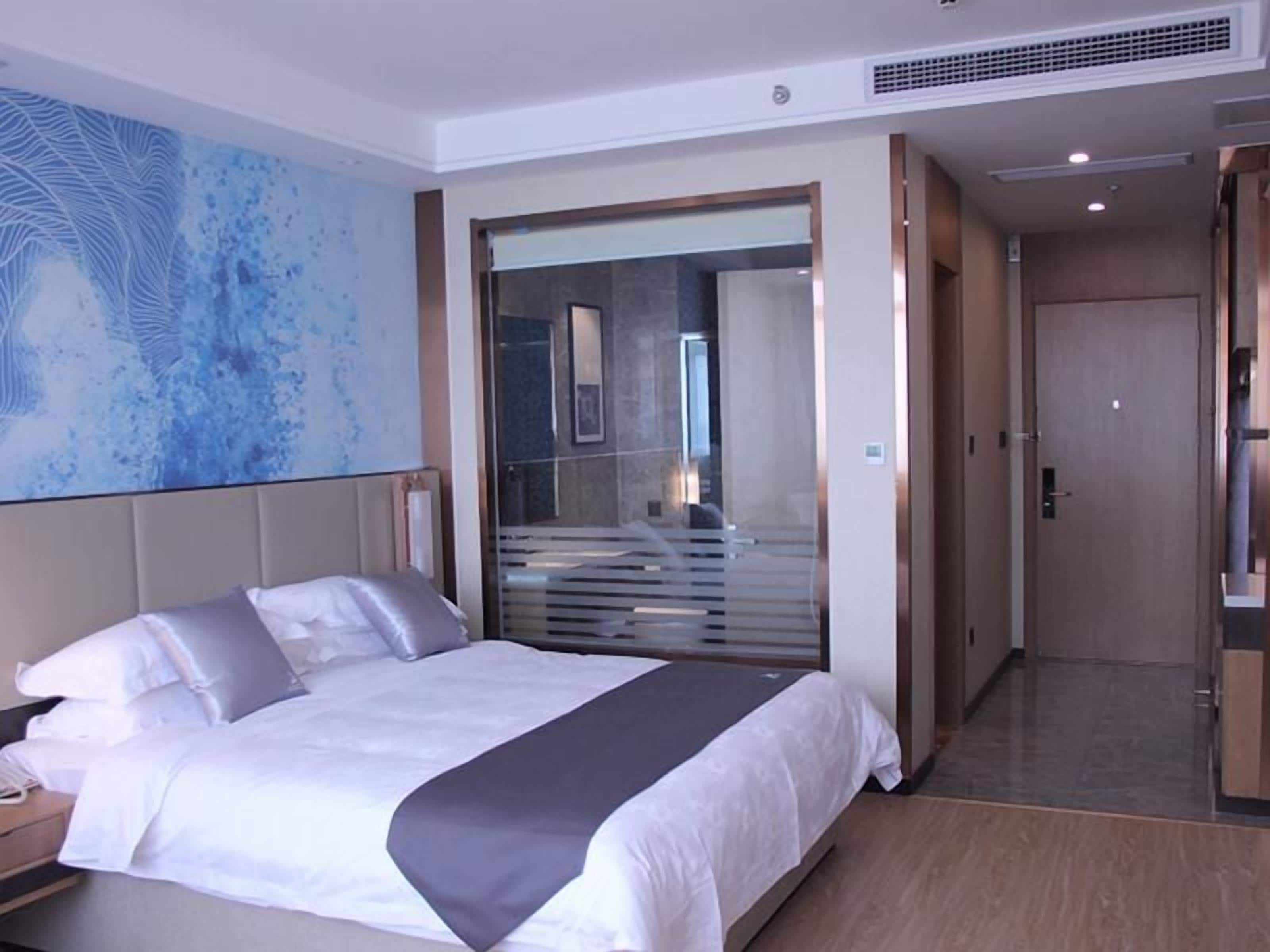 A hotel room with a bed, a nightstand, a large mirror, and a view of a staircase.