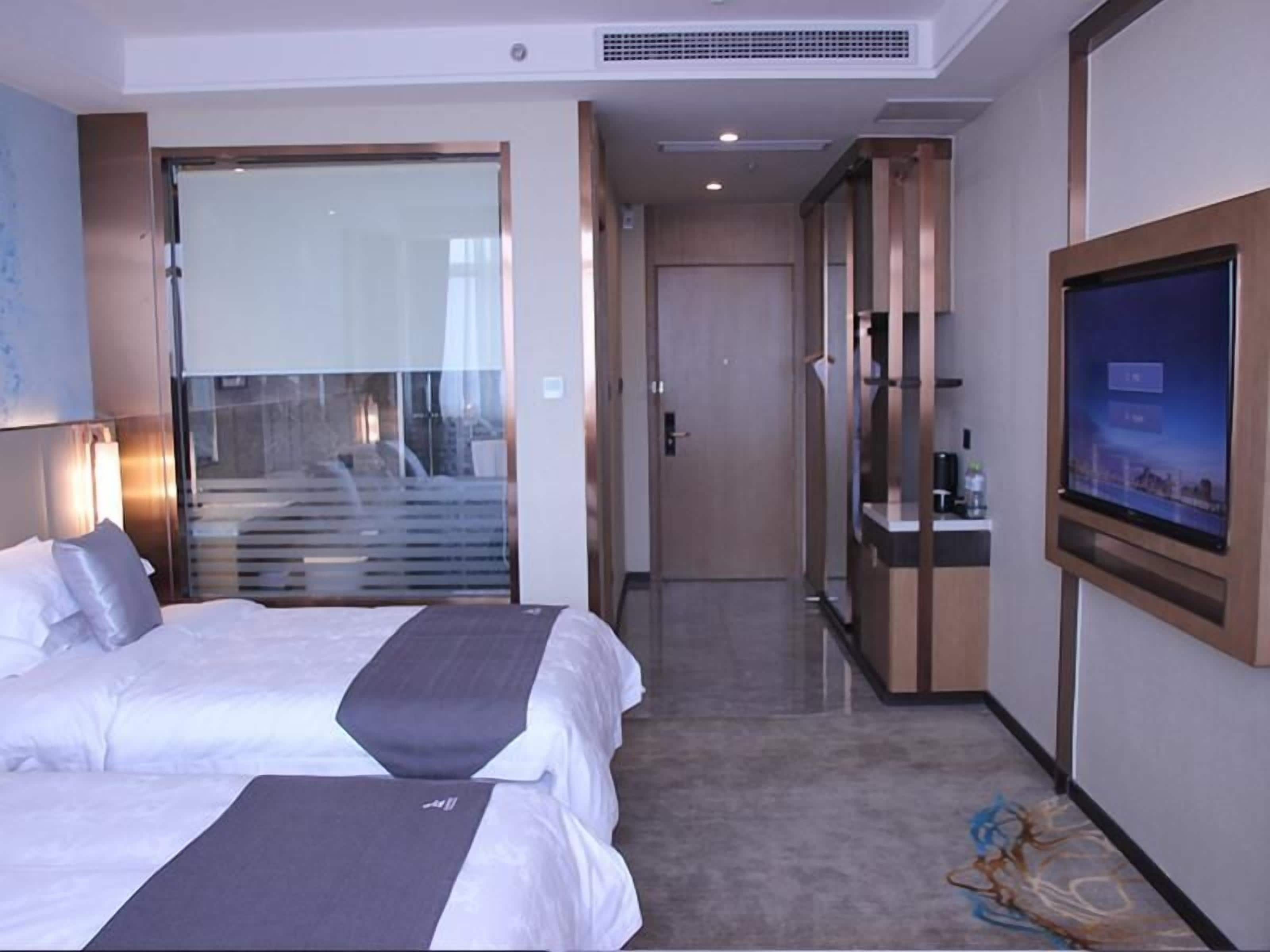 Habitación de hotel con cama, televisión y puerta de vidrio que da a un balcón.