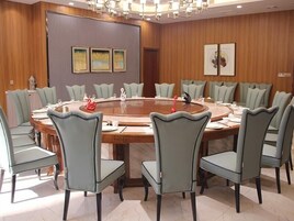 A conference room with a round table, grey upholstered chairs, and wooden paneling on the walls.