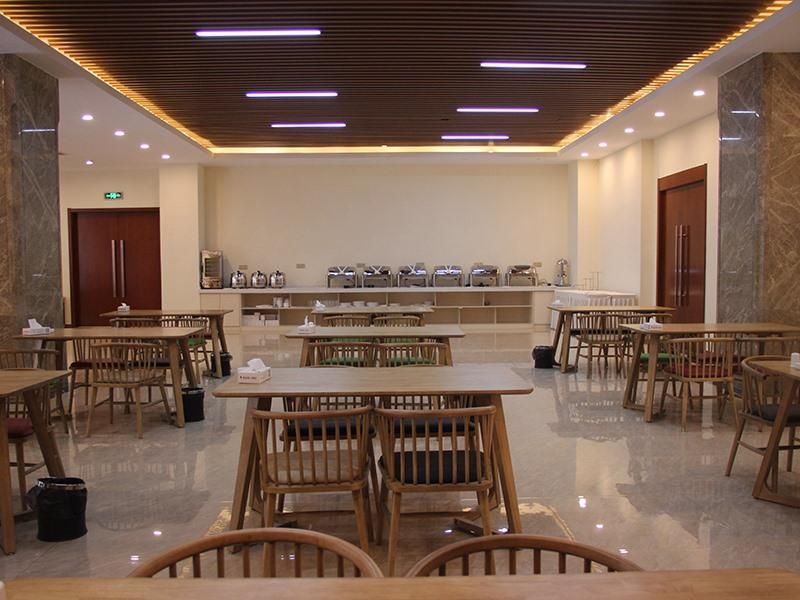 A spacious dining area with wooden tables and chairs, a marble floor, and a modern ceiling with linear lighting.