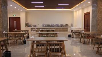 A spacious dining area with wooden tables and chairs, a marble floor, and a modern ceiling with linear lighting.