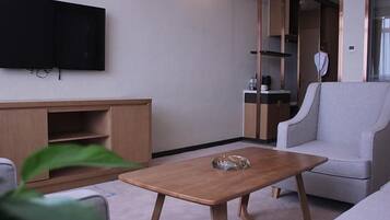 A modern living room with a flat-screen TV, a wooden coffee table, a grey sofa, and a built-in wardrobe.