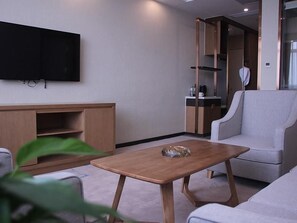 A modern living room with a flat-screen TV, a wooden coffee table, a grey sofa, and a built-in wardrobe.