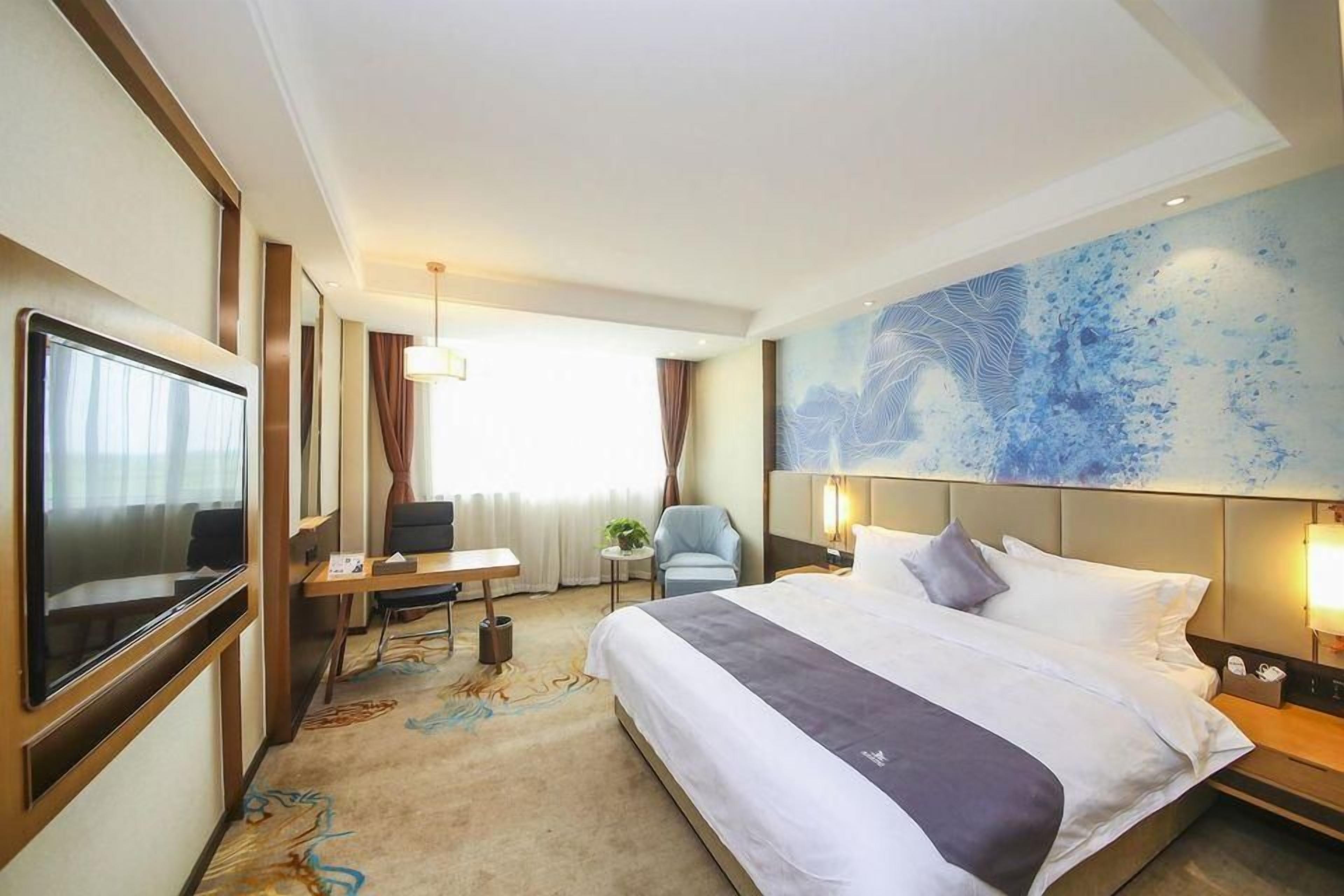 A hotel room with a bed, a desk, a television, and a large abstract painting on the wall.