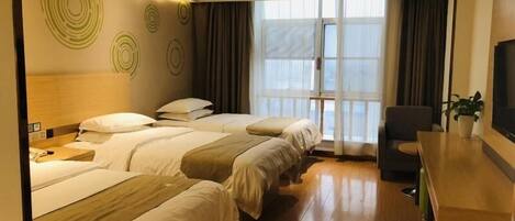 A hotel room with three beds, a wooden desk, a television, and a large window with curtains.