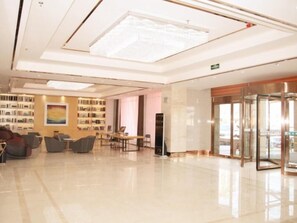 A modern lobby with a glass elevator, seating area, and a bookshelf.