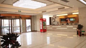 A spacious lobby with a reception desk, a vending machine, and a large glass door leading outside.