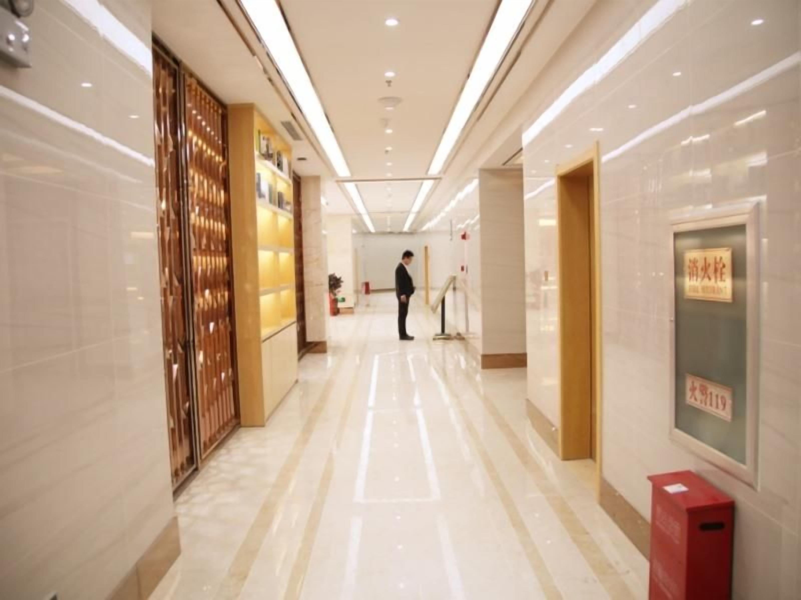 A hotel corridor with a polished floor, a reception area, and a person standing in the distance.